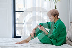 a woman in a green suit and with a phone in her hands sits on a large bed