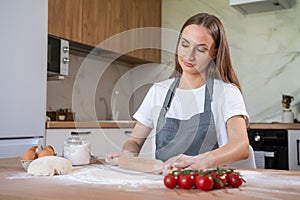 Woman in a grey chef& x27;s apron roll out the dough for preparing pancake. Woman rolls out dough