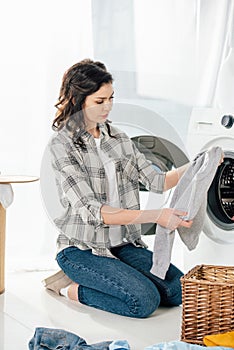 woman in grey shirt and jeans holding clothes near washer