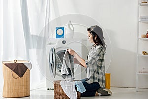 woman in grey shirt and jeans putting clothes in basket near washer