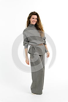 Woman in grey sweater and wide leg pants, styling her hair with a smile