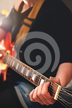 Woman grips chord on electric solidbody guitar with cherry sunburst body.