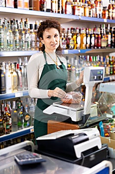 Woman grocery store clerk weighs sausages on scale