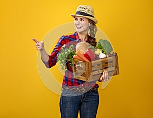 Woman grower with box of fresh vegetables pointing at something