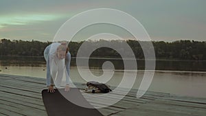 Woman Grows a Yoga Mat on Wooden Wharf on the Background of the Morning River