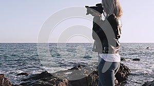 Woman in grunge style taking pictures of sea with DSLR camera.