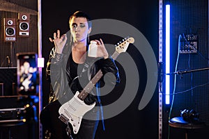 Woman guitarist holding bottle of drugs showing medicament at camera during music lesson in sound studio