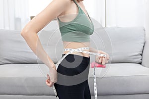 Woman in a gym clothes uses a centimeter strap to measure her circumference thin waist