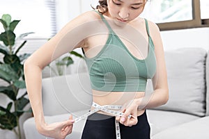 Woman in a gym clothes uses a centimeter strap to measure her circumference thin waist