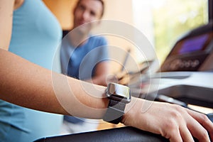 Woman In Gym With Personal Trainer Analysing Performance Using Smart Watch And Digital Tablet