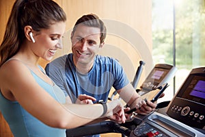 Woman In Gym With Personal Trainer Analysing Performance Using Smart Watch And Digital Tablet