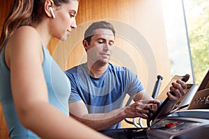 Woman In Gym With Personal Trainer Analysing Performance Using Smart Watch And Digital Tablet