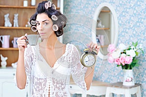 Woman in hair curlers with coffee and clock in the morning