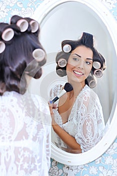 Woman in hair curlers puts on morning makeup