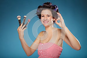 Woman in hair rollers holds makeup brushes