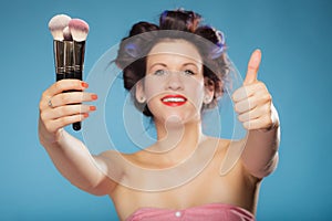 Woman in hair rollers holds makeup brushes