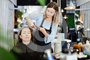 Woman hair stylist making haircut to aged female client