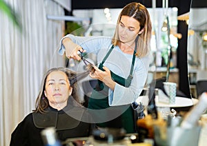 Woman hair stylist making haircut to elderly female client