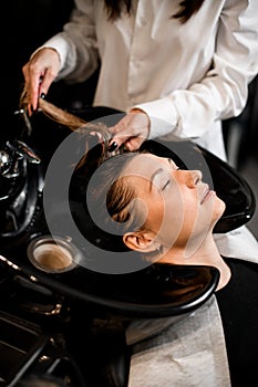 woman on hair washing chair with her eyes closed and hands of hairdresser washing her hair.