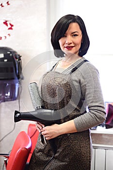 Woman hairdresser with black hair with hairdryer and brushing in the hairdressing salon