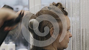 A woman hairdresser dries her hair with an electric hair dryer.