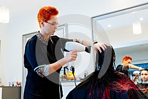 Woman hairdresser drying young woman customer hair in salon