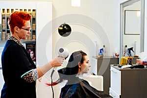 Woman hairdresser drying young woman customer hair in salon