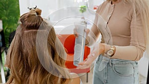 Woman hairdresser stylist makes hairstyle blonde. Special varnish for fixing hair in a spray bottle.