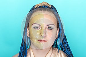 Woman half face in a mask of green clay on a blue background.