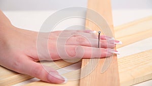 A woman hammers a nail with a hammer in a wooden construction. hands with beautiful manicure close-up.