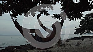 A woman in a hammock on the beach with a phone.