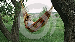 Woman in hammock is blows bubbles outdoors. Young girl in hat and dress lying in hammock and blowing bubbles, resting and relaxin