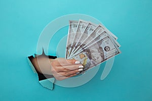 A woman hand appears in the hole in torn blue paper and squeezes dollar bills. The concept of alimony poverty, benefits