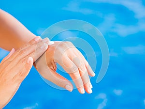 Woman hand apply sunscreen / sunblock by the swimming pool.
