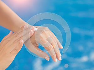 Woman hand apply sunscreen / sunblock by the swimming pool.