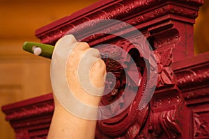 Woman hand with big brush painting wooden cupboard with splendid handmade carved ornaments in red color in workshop for