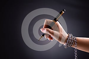 Woman hand with black pen tied with chain, depicting the idea of freedom of the press or freedom of expression on dark background