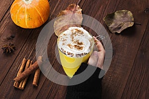 Woman hand in black sweater holding a cup of pumpkin latte with