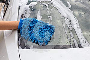 Woman hand with blue microfiber fabric washing rear mirror modern car or cleaning automobile.