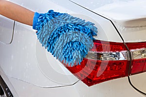 Woman hand with blue microfiber fabric washing taillight modern car or cleaning automobile.