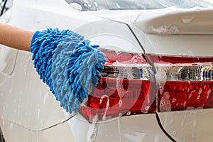 Woman hand with blue microfiber fabric washing taillight modern car or cleaning automobile.