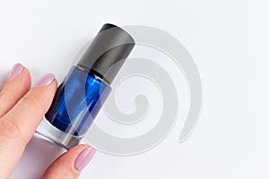 Woman hand with blue nail polish bottle on white background