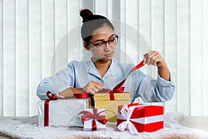 Woman hand in a blue shirt opening a gold gift box tied with a red ribbon present for the festival of giving special holidays like