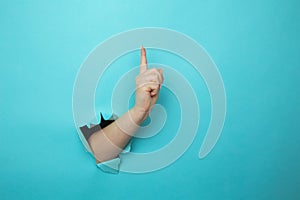 Woman hand breaking through blue paper wall with finger point up