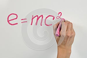 Woman hand with bright pink chalk writing mass-energy equivalence formula on white desk or wall photo
