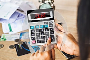 Woman hand calculating her expenses with unpaid financial bills ,credit cards on desk with word debt on calculator