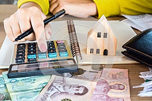 Woman hand calculating money paper currency with house model and calculator on desk, planing to buy or rent home , payment for