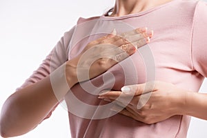 Woman hand checking lumps on her breast for signs of breast cancer on gray background. Healthcare concept