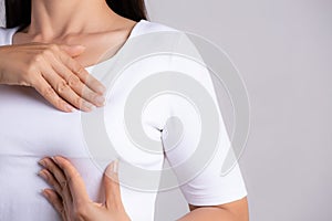 Woman hand checking lumps on her breast for signs of breast cancer on gray background. Healthcare concept