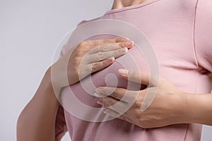 Woman hand checking lumps on her breast for signs of breast cancer on gray background. Healthcare concept